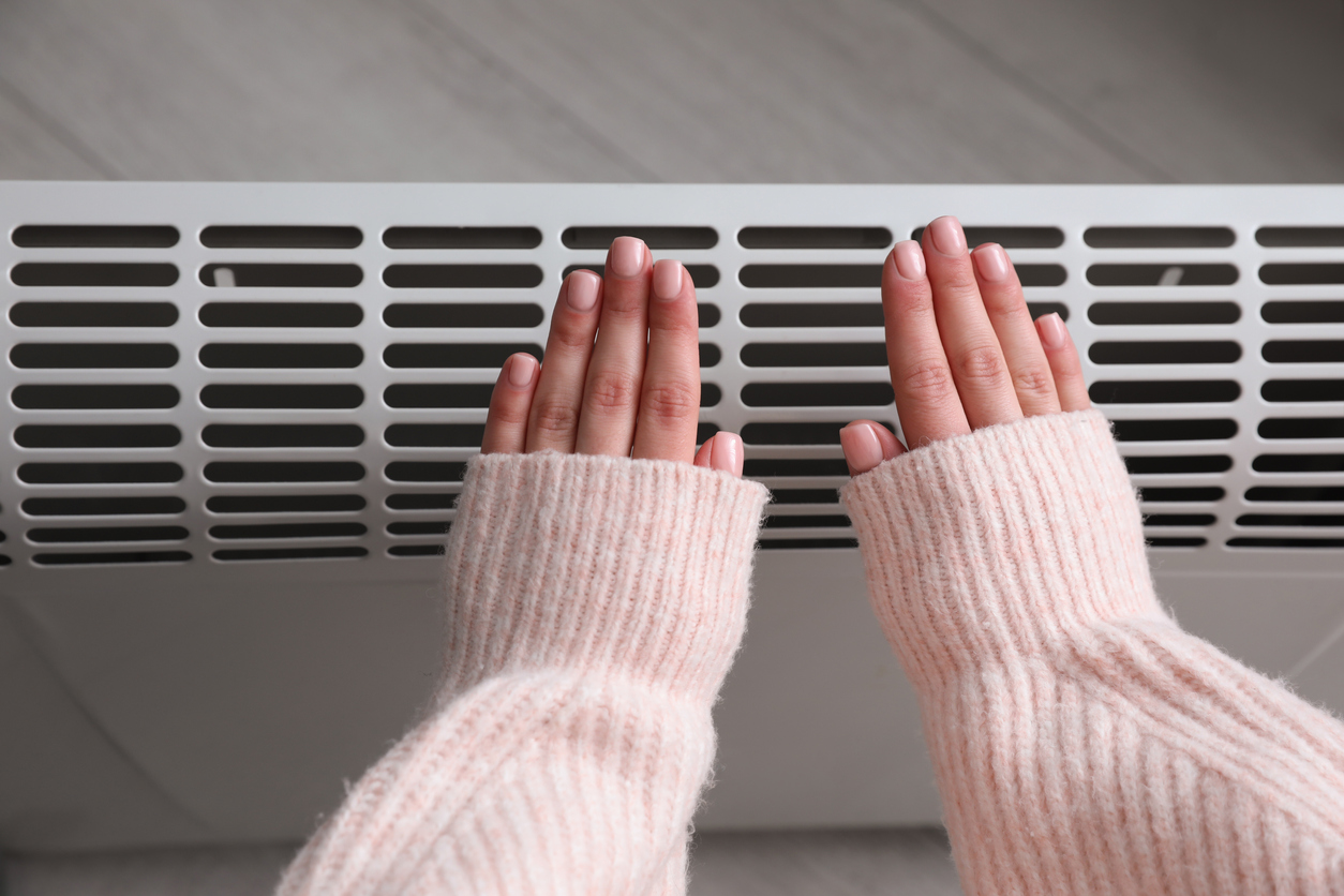 Woman warming hands near electric heater at home, hydro air